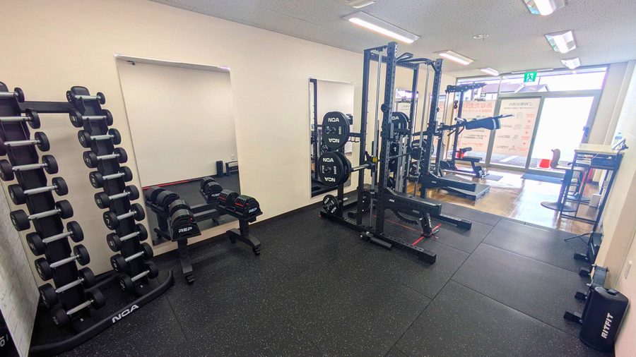 GYM BASE 伝法店の店内全体。貸切の筋トレルームに、左にダンベルラック、中央にパワーラック、奥に窓と入口、床は黒いトレーニングマット